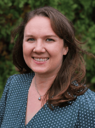 Smiling woman with brown hair, outdoor background.