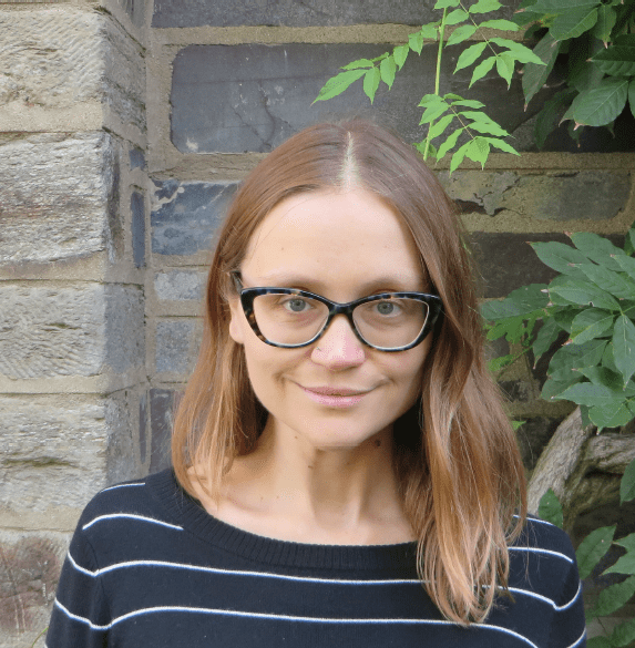Woman with glasses in front of stone wall.