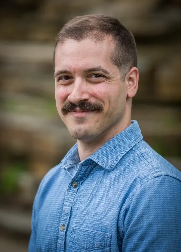Man with mustache in blue shirt smiling.