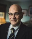 Smiling bald man wearing glasses, suit, and tie