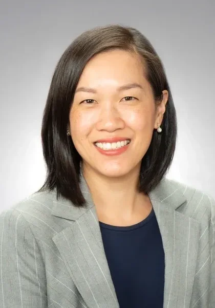 Smiling person in a gray suit jacket.