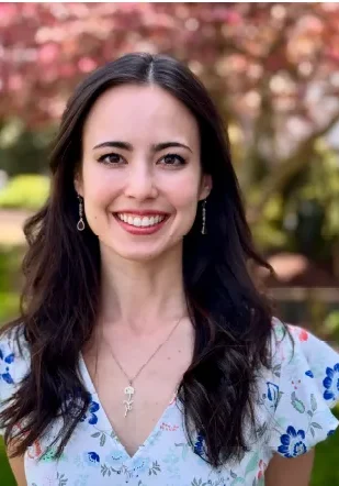 Smiling woman outdoors with floral background.
