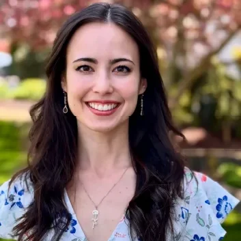 Smiling woman outdoors with floral background.