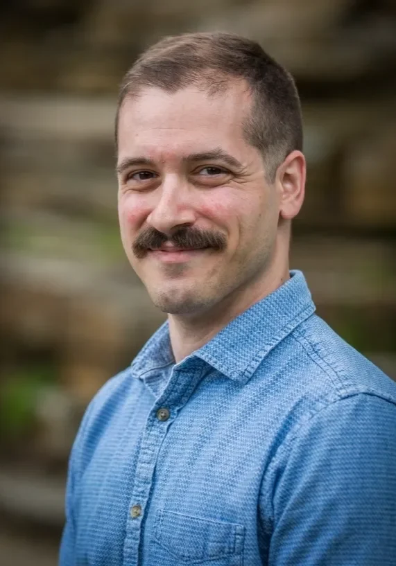 Man with mustache in blue shirt smiling.