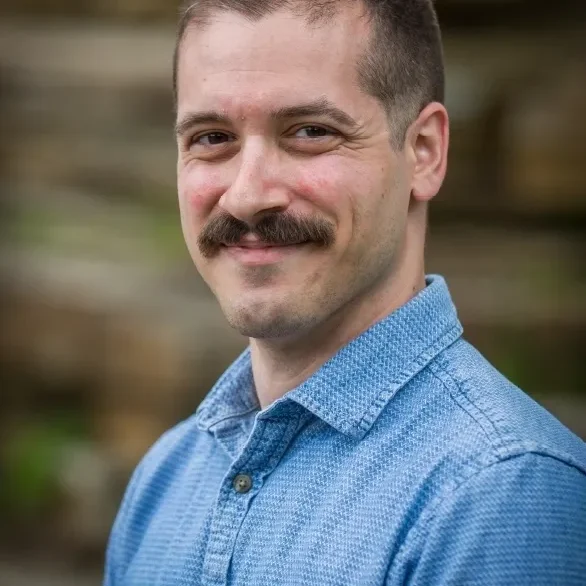 Man with mustache in blue shirt smiling.
