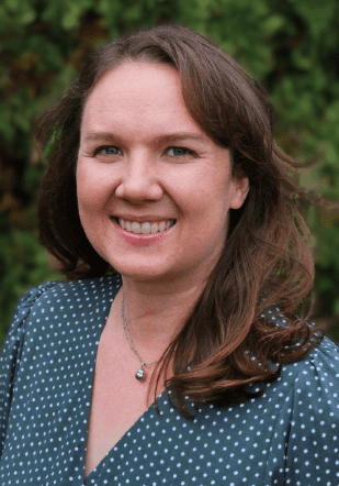 Smiling woman with brown hair, outdoor background.