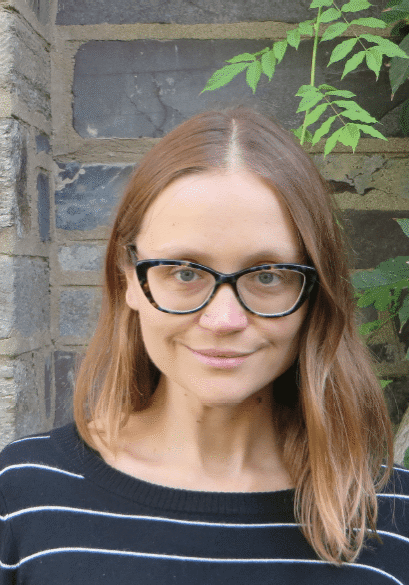 Woman with glasses in front of stone wall.